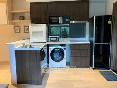 Modern kitchen with sleek appliances and wooden cabinetry, featuring a washing machine and microwave.