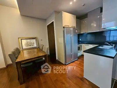 Modern kitchen with sleek cabinetry and dining area, featuring hardwood floors and stainless steel appliances.