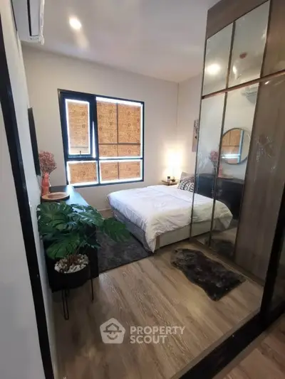 Cozy bedroom with modern decor, large mirrored wardrobe, and natural light from window.