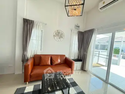 Modern living room with leather sofa, stylish chandelier, and large windows offering natural light.