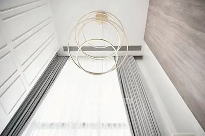 Elegant modern interior with high ceiling and stylish chandelier, featuring floor-to-ceiling curtains and wood accents.