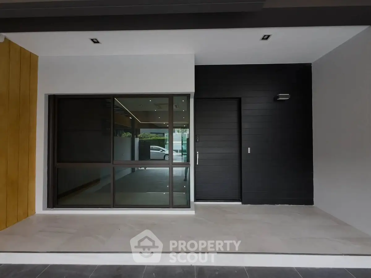 Modern home entrance with sleek black door and large window, showcasing contemporary architectural design.