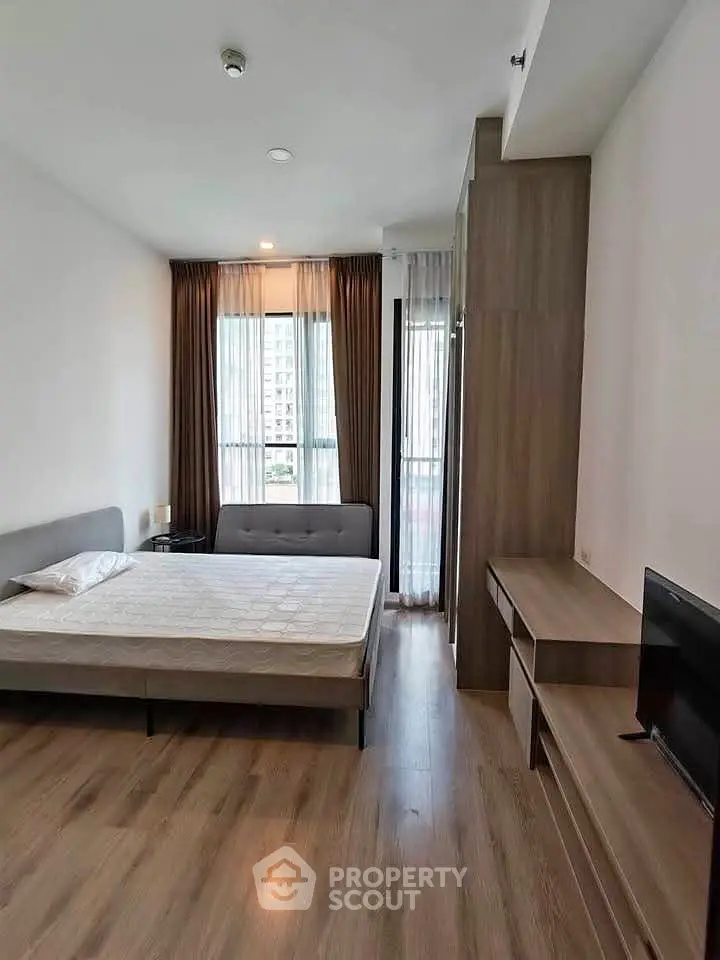 Modern bedroom with wooden flooring and large window in a stylish apartment.