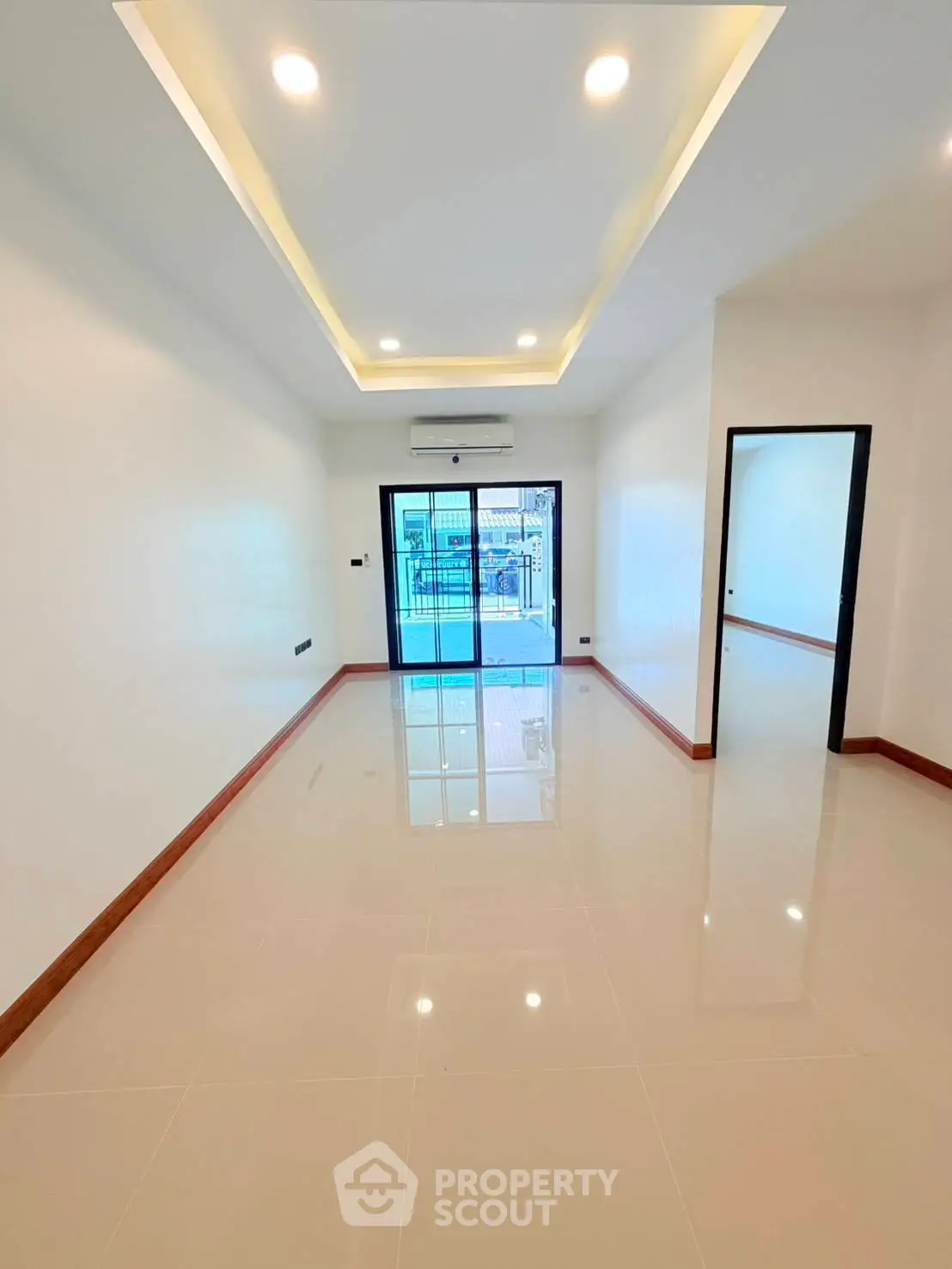 Spacious modern living room with sleek tile flooring and recessed lighting, leading to a balcony with a view.