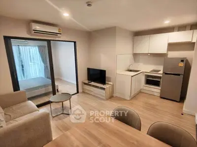 Modern open-plan living room with kitchen and bedroom view, featuring sleek furniture and wooden flooring.