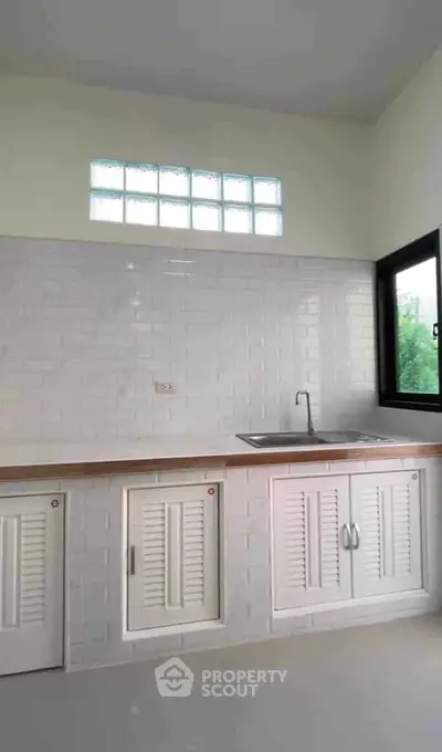 Modern kitchen with white cabinetry and sleek countertop, featuring a large window for natural light.