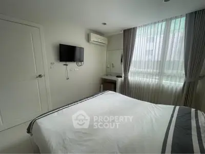 Modern bedroom with minimalist decor, featuring a wall-mounted TV and large window for natural light.