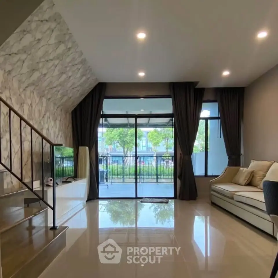 Spacious living room with modern design and large windows overlooking greenery.