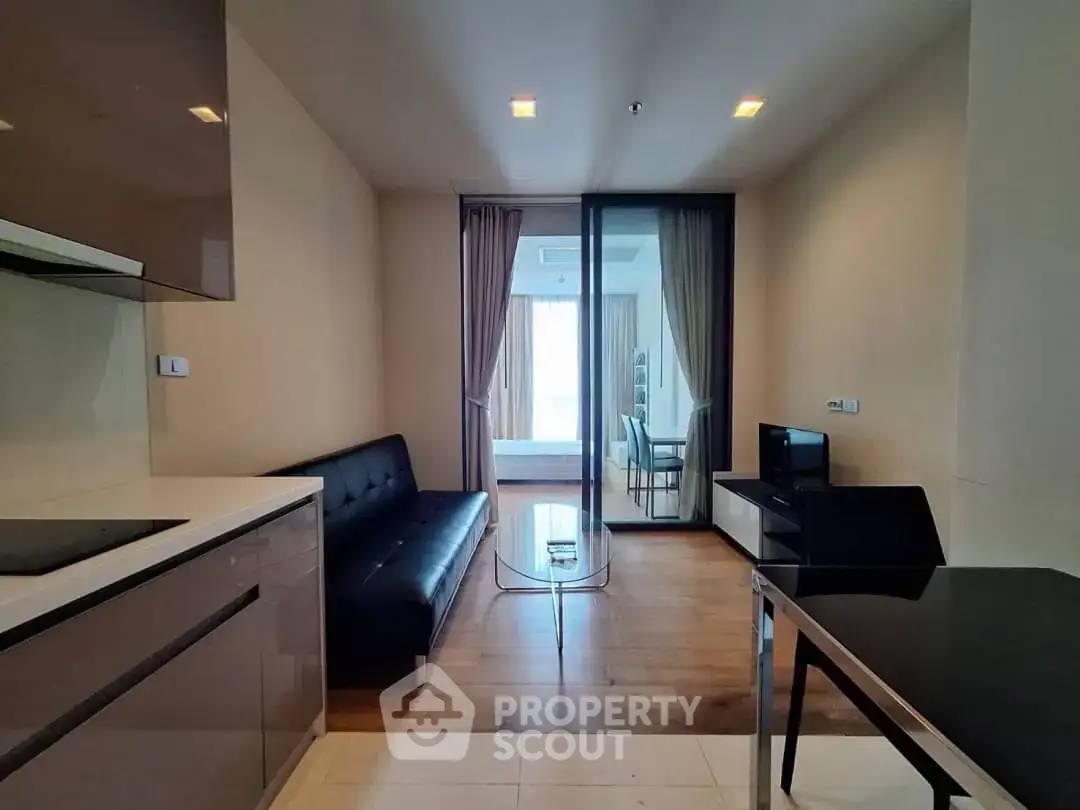 Modern apartment interior with sleek kitchen and cozy living area, featuring a glass partition and stylish furnishings.