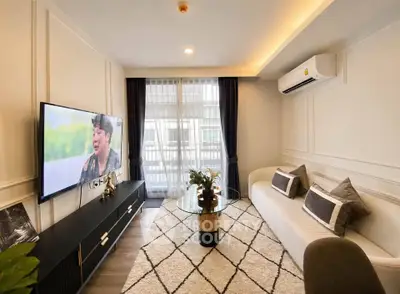 Modern living room with stylish decor, large TV, and natural light from window.