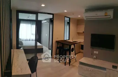 Modern open-plan living room with kitchen and bedroom view, featuring sleek furniture and air conditioning.