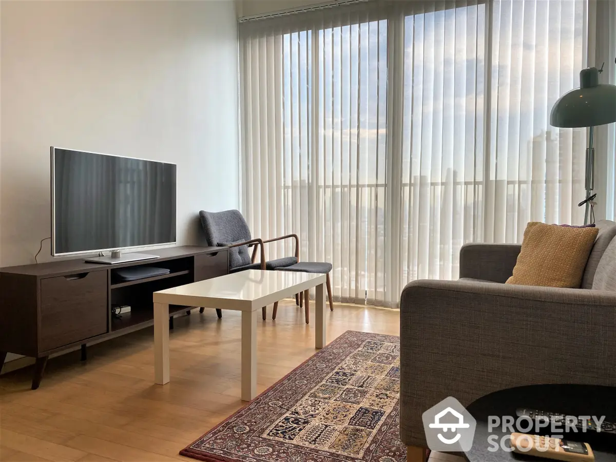 Spacious living room with modern furniture, large windows draped with sheer curtains, and a classic area rug, creating a warm and inviting atmosphere.