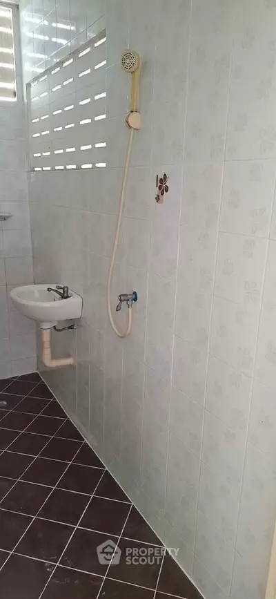 Compact bathroom with tiled walls and floor, featuring a wall-mounted sink and showerhead.