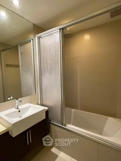 Modern bathroom with sleek sink and shower over bathtub in elegant design.