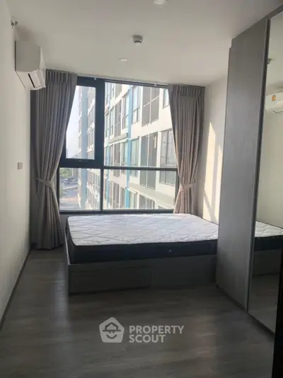 Modern bedroom with large window and minimalist design in urban apartment.