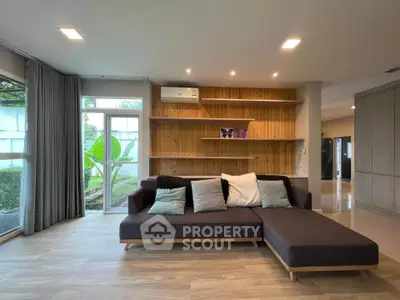 Spacious modern living room with stylish sofa and wooden shelving, featuring large windows for natural light.