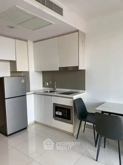 Modern kitchen with sleek white cabinets, stainless steel fridge, and cozy dining area.