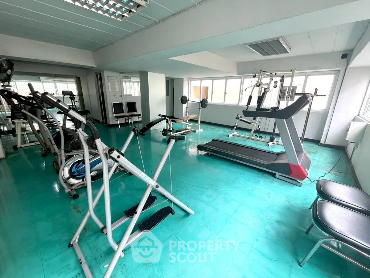 Spacious gym with modern fitness equipment and bright turquoise flooring.