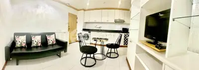 Modern living room with open kitchen, featuring sleek black furniture and built-in appliances.