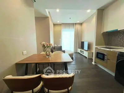 Modern open-plan living room with dining area and kitchen, featuring sleek furniture and natural light.