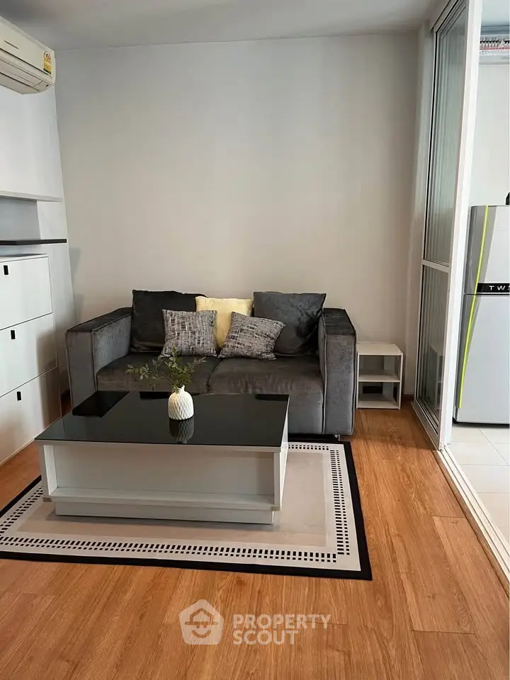 Modern living room with sleek sofa, glass coffee table, and wooden flooring in a cozy apartment.