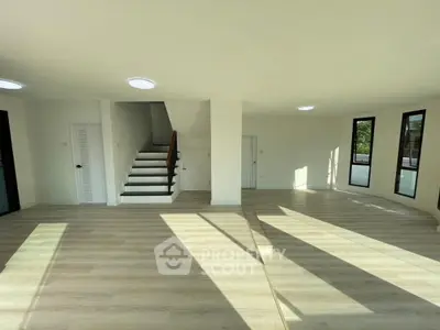 Spacious sunlit living room with modern staircase and large windows.