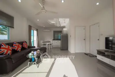 Spacious living room with modern decor and natural light, featuring a cozy seating area and sleek kitchen.