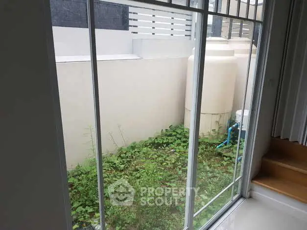 Modern home window view with small garden area and water tanks