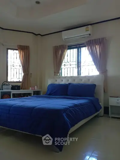 Cozy bedroom with blue bedding and natural light, featuring air conditioning and elegant curtains.