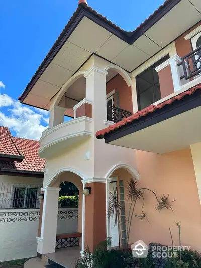 Charming two-story house with red-tiled roof and elegant balcony in a serene neighborhood.