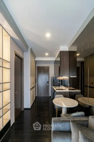 Modern apartment interior with sleek kitchen and cozy living area, featuring dark wood flooring and stylish furnishings.