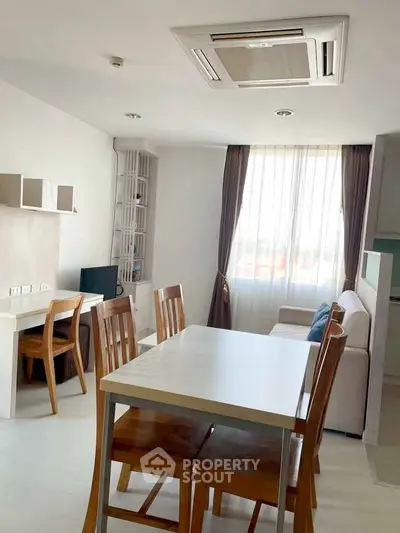 Bright modern living room with dining area and large window, featuring wooden furniture and neutral decor.
