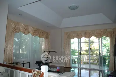Spacious living room with polished floors, elegant drapery, and ample natural light, leading to a sunlit balcony with greenery views.