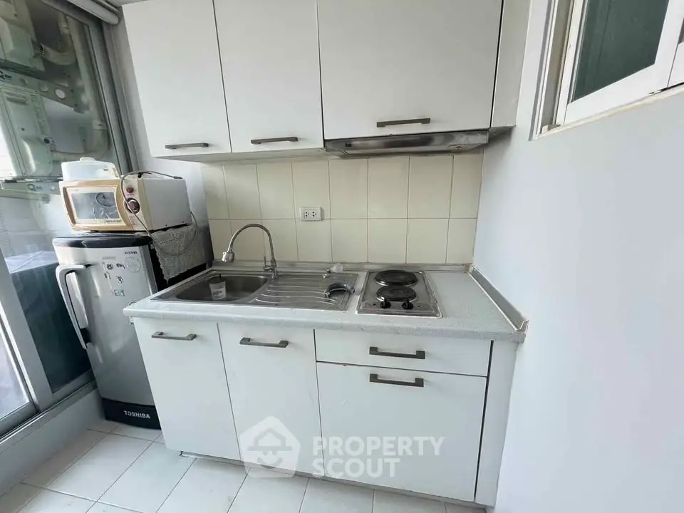 Compact kitchen with white cabinets and modern appliances in cozy apartment