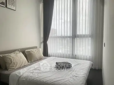 Cozy bedroom with large window and elegant curtains, featuring a neatly made bed with soft pillows.