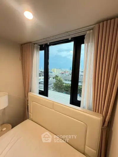 Cozy bedroom with large window offering a stunning city view, perfect for urban living.