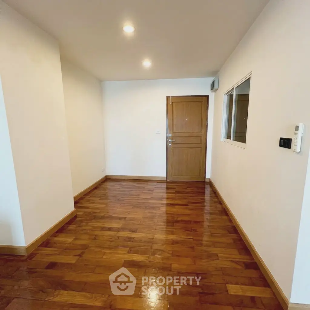 Spacious entryway with polished wooden floors and modern lighting in a contemporary apartment.