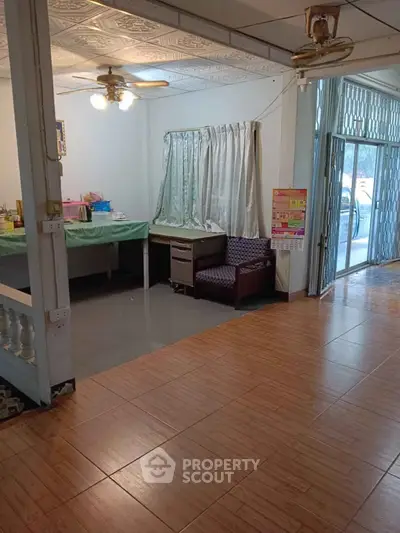 Spacious living area with tiled flooring and ceiling fan, featuring a cozy seating corner and ample natural light.