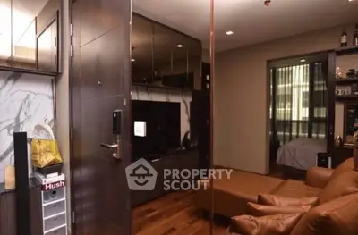 Modern living room with leather sofa and TV, open view to bedroom, sleek wooden flooring.