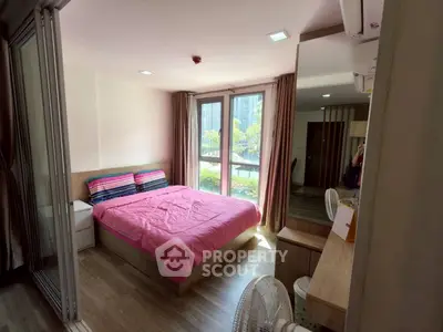Cozy bedroom with pink bedding, large windows, and modern decor in a bright apartment.