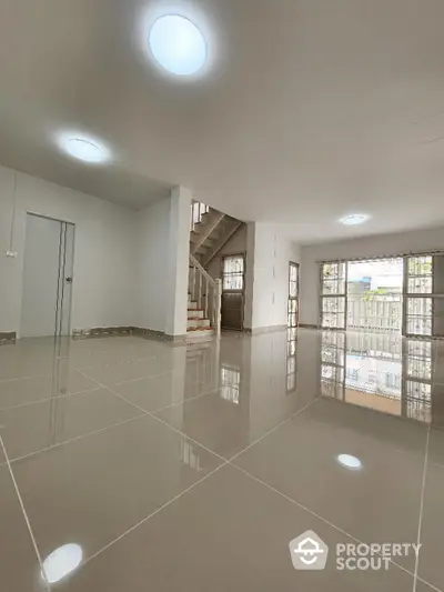 Spacious and bright living area with glossy tiled flooring, modern recessed lighting, and an elegant staircase leading to the upper level, perfect for luxurious living.