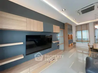 Modern living room with sleek wooden cabinetry and large TV, featuring stylish lighting and air conditioning.