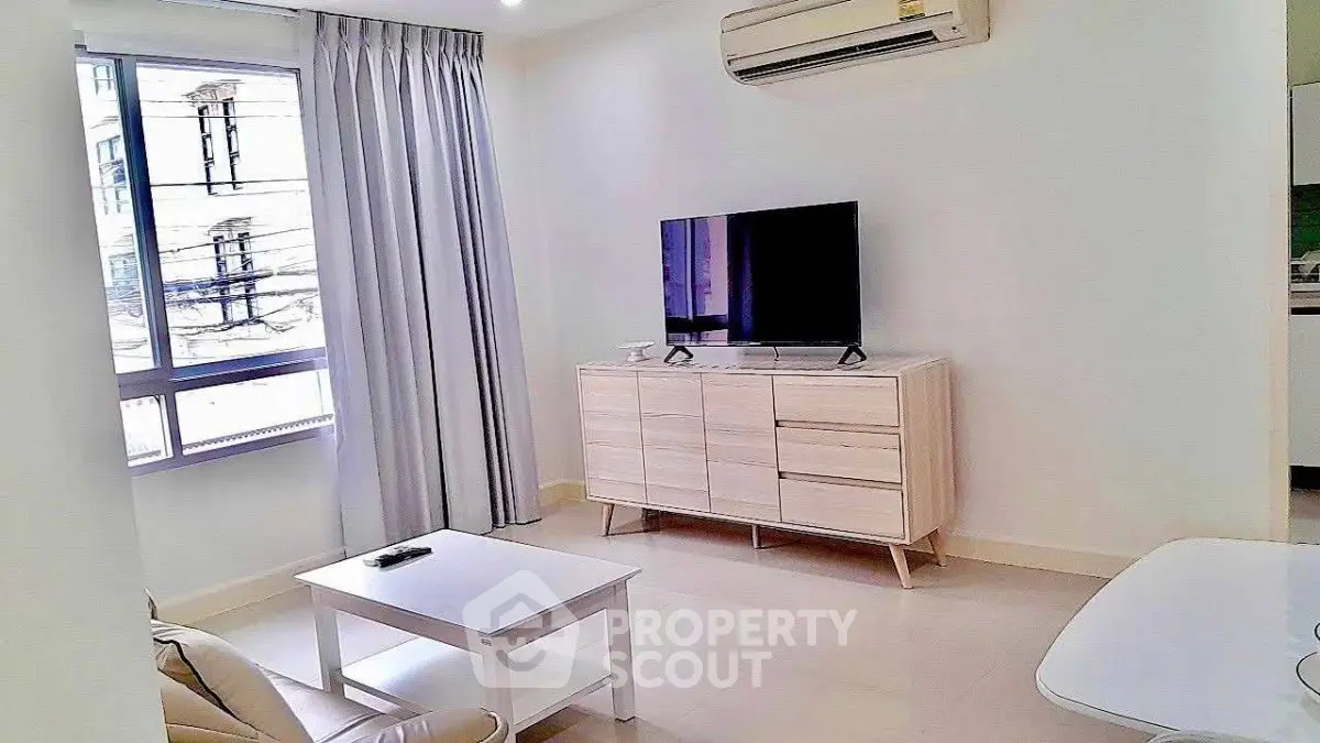 Modern living room with sleek furniture and natural light, featuring a TV and air conditioning.