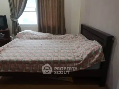 Cozy bedroom with wooden bed frame and patterned bedspread, natural light from window.
