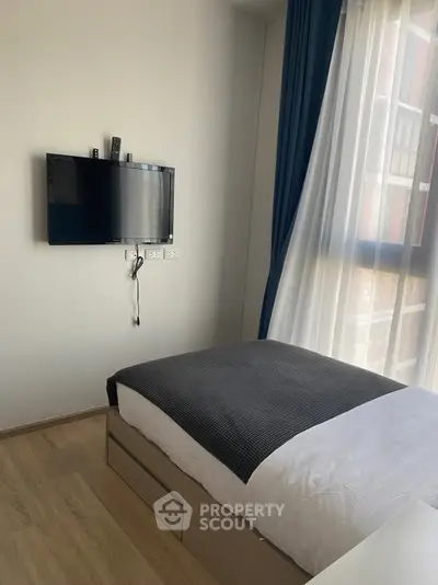 Modern bedroom with wall-mounted TV and large window with blue curtains.