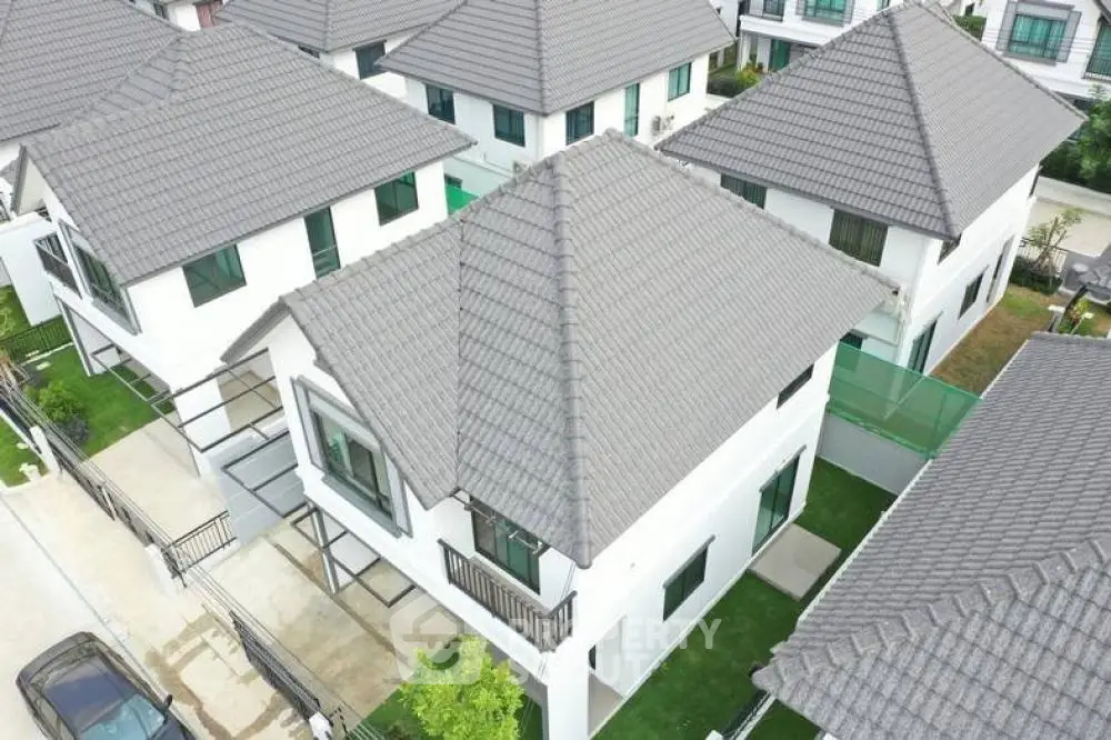 Aerial view of luxurious suburban homes with pristine white exteriors, grey tiled roofs, and well-manicured lawns, showcasing upscale living in a serene neighborhood.