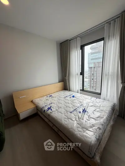 Modern bedroom with large window and city view, featuring a neatly made bed and minimalist decor.