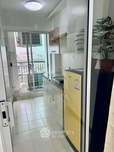 Compact kitchen with balcony view, featuring yellow fridge and modern appliances in a bright, airy space.