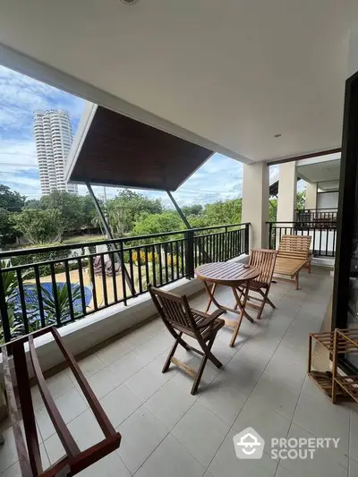 Spacious balcony with wooden furniture and scenic view of greenery and tall building.