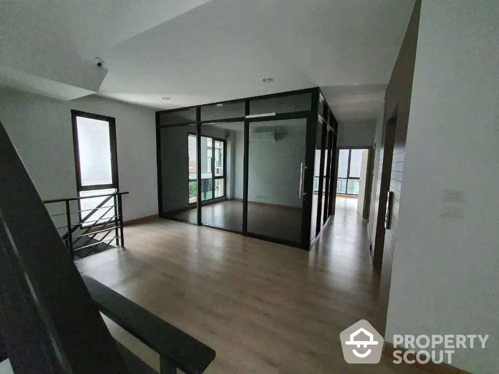 Spacious and modern living area with abundant natural light, featuring sleek wooden flooring and a sophisticated glass partition, perfect for contemporary living.